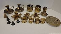 Full view of brass items set including candlesticks, napkin rings, bells, and trivet.