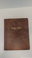 Closed brown 'CANADA CENTS 1920' coin book with gold lettering on cover.