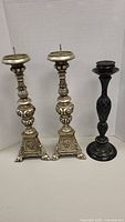 Three candlesticks shown side by side; two matching ornate Berman candlesticks with crackle finish and one black simpler metal candlestick.