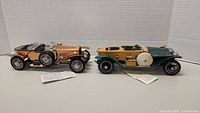 Two Franklin Mint car models displayed side by side, the copper colored 1921 Rolls Royce Silver Ghost on the left and green beige 1914 Rolls Royce on the right