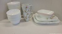 Set of stacked white Corelle plates, white bowls, mugs with floral design, pink-rimmed square bowls