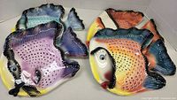 Four colorful fish-shaped ceramic wall decor plates with detailed scale textures and vibrant paint. Each plate is signed on the back by Ryan Charles.