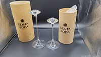 Pair of Kosta Boda glass candlesticks with branded packaging tubes, displaying overall size and shape.