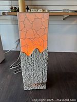 Stone lighted stand illuminated showing orange glow on the top section with rough base.