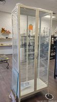 Front view of white metal frame display cabinet wrapped in plastic film.