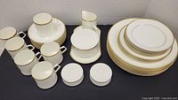 Full set arranged with stack of plates, cups, cream pitcher, sugar bowl with lid on oval tray, and salt and pepper shakers