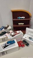 Overview of eleven Franklin Mint metal model cars arranged with display rack and packaging boxes