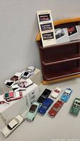 12 model cars arranged in front of wooden display rack with boxes and instruction cards