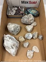 Overview of multiple quartz rocks of varying sizes, small tray with quartz crystal pieces, and an iridescent abalone shell inside a cardboard box.