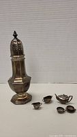 Photo showing tall octagonal sterling silver container with pierced lid and miniature tea set including small teapot, creamer, sugar bowl, and two cups.
