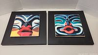 Two square ceramic photo tiles mounted on wood, each depicting colorful totem pole faces, side by side.