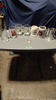 Overview of eight beer mugs and one opener on table showing brands and variety