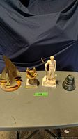Four items on table: two brass sailboat figurines, a carved stone sculpture, an ornate brass floral decorative piece, and a brass inkwell