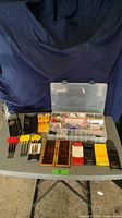 Wide view of the lot showing multiple dart cases, 4 complete dart sets, and a large plastic compartment box with various components.