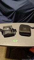Two binocular carrying cases, one soft with a flap and white circular logo, one hard and zippered with Vortex logo, sitting on a gray table.
