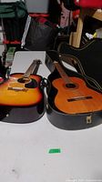 Two acoustic guitars side by side on table with hard case behind