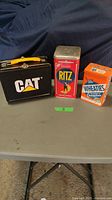 CAT lunch box with two vintage tins on a grey table with a blue backdrop