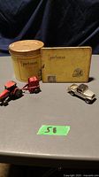 Photo showing the four items including a red die cast Case tractor, a silver Hot Wheels Jeep Scrambler, the flat yellow Sportsman tobacco tin, and the round yellow Sportsman tobacco tin, all placed on a grey surface.