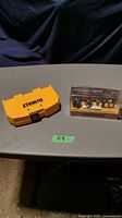 Two closed cases on a table: yellow DeWalt branded concrete bit set and clear-topped orange Mastercraft router bit set.
