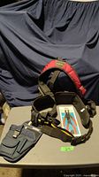 Adjustable suspender/back support tool belt with tool storage compartments and red padded straps, shown laid out on table.