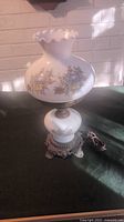 Full view of the antique glass globe table lamp with metal base and floral decorative designs. Lamp cord visible along with the scalloped rim upper glass globe.