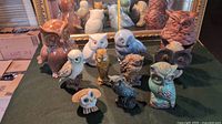 Eleven owl figurines arranged on a dark cloth; varying styles, colors, and sizes from about 6 to 12 inches tall.