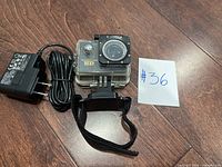 Image of Cobra Adventure HD camera in waterproof case with charger and strap mount on wooden floor.