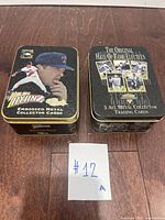 Two metal boxes for collector baseball cards. One features Nolan Ryan in Texas Rangers uniform with embossed metal design. The other box is titled 'The Original Hall of Fame Electees' with five metal collector trading cards.