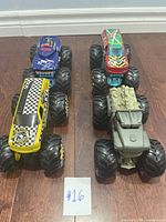 Four large monster trucks on wooden floor, two front and two rear, showing size and design variety.