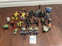 Overall view of all 20 assorted action figures laid out on the floor, showing variety in style and color.