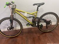 Side profile of the yellow-green Columbia mountain bike showing tires, frame, pedals, suspension coil, and handlebar with green grips.