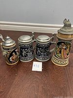 Four vintage German beer steins with metal lids arranged on wood floor, showing different styles and sizes