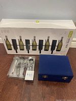 Photo showing white box containing Taoy wine rack, wine tasting accessory set in plastic, and blue hinged box.