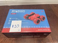 Sealed boxed ZingZoom Remote Control Stunt Car model K-02 in red on dark wood surface with #10A sticker.