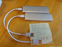 Two silver external SSDs with attached white cables displayed on table