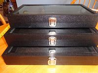 three stacked black glass-top display cases showing front latches