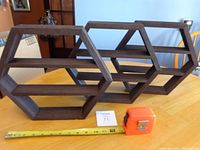 Three dark brown hexagon wooden shelves on table with tape measure for scale