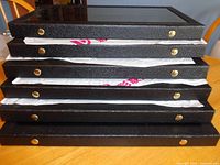 Stack of six black display cases showing brass snaps and protective wrap