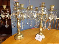 Both matching gold-tone candelabra on table showing overall design and acrylic prisms