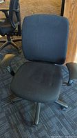 Front view of the black office chair showing padded seat and backrest, armrests, and wheel base.