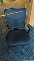 Front view of black mesh office chair with padded seat and adjustable armrests on carpeted floor.