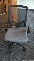 Front view of adjustable office chair showing mesh back and padded grey seat with black armrests and wheeled base.