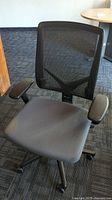 Front view of a black mesh back office chair with padded seat and adjustable armrests on caster wheels, showing the seat and backrest.