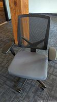 Front view showing black mesh backrest and gray padded seat with armrests on a rolling base.