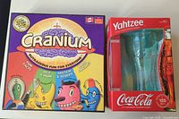 Photo of Cranium and Yahtzee board games in original boxes. Cranium box depicts cartoon characters and game activity types. Yahtzee box is red Coca-Cola 125th Anniversary Collector's Edition with dice and cup visible.