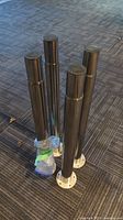 Four Olov IKEA metal table legs standing upright on carpet, showing round base plates and mounting hardware bag attached.