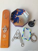 Photo of all items shown including wooden bottle opener, Nerf darts, novelty beer bell, metal ring toss game pieces, fidget toy
