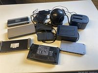 Full lot of miscellaneous computer equipment arranged on white table, showing multiple docking stations, hard drive docks, and network switch devices with cables.