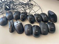 Top view of 14 assorted computer mice, black/dark colors, wired and wireless mixed, various brands including Lenovo, HP, Logitech, Dell, Targus, Anker, Brookstone