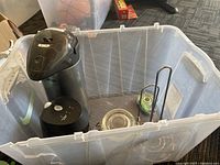Plastic storage container with kitchen items inside including electric coffee maker, glass jar with lid, coffee thermos, and a black metal paper towel holder